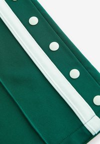 Tissu vert avec une rayure blanche et cinq grands boutons ronds blancs le long du bord ; texture lisse avec un design ajusté.