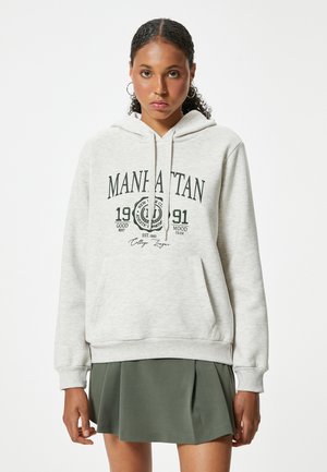 Sudadera gris claro hecha de una tela suave, con un bolsillo tipo canguro, capucha con cordón y un gráfico de texto negro que dice "MANHATTAN".