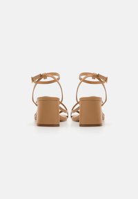 Brune blokkhælte sandaler med flere remdesigns og ankelspænde, glat læderfinish og en robust hæl for støtte.