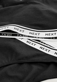 Sort bomuldsstof med hvid elastikbånd med "NEXT" tekst. Glat tekstur, strækbar design, afslappet stil for komfort.