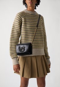 Zwarte leren schoudertas met een kettingriem, voorzien van een glimlachend palmboomontwerp. Gemaakt in combinatie met een gebreid gestreept sweater en een geplooide rok.