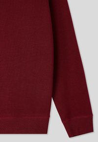 Felpa bordò con una texture liscia, polsini e orlo a coste. Il tessuto appare morbido e spesso, caratterizzato da dettagli di design minimalisti.