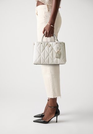 Borsa bianca trapuntata con una finitura testurizzata, hardware in tono oro e un accento con portachiavi. Indossata con jeans cropped avorio e tacchi a spillo neri.