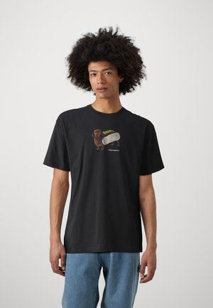 Black cotton t-shirt featuring a graphic of a dachshund as a sushi roll, with green accents and a relaxed fit. Plain background.