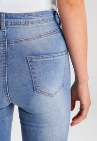 Höga ljusblå jeans med en figursydd design, som har en enda bakficka och synliga sömdetaljer. Slät denimtextur.