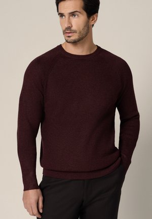 Bordowy sweter z okrągłym dekoltem, o prążkowanej fakturze, z długimi rękawami i dopasowanym dołem. Tkanina wydaje się miękka i lekko fakturowana.