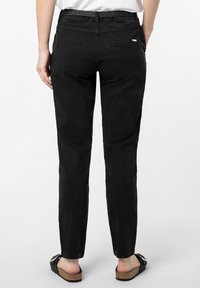 Zwarte slim fit broek met een gebreid tailleband en twee achterzakken. Draagt bij platte zwarte sandalen op een lichte achtergrond.