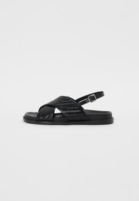 Sorteve svartvevd sandal med kryssbånddesign, justerbar ankelrem og flat gummisåle. Teksturert materiale med glatt finish.