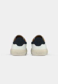 Pair of white low-top sneakers with beige soles and black heel accents, shown from the back on a white background.