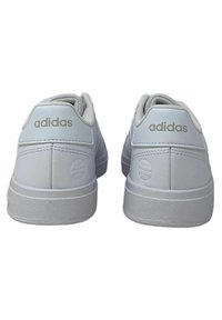White Adidas sneakers with a textured leather upper, padded collar, and light gray rubber sole. "Adidas" logo featured on the heel tabs.