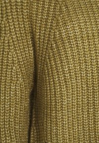 Stickad tröja i dämpad olivgrön, med ett strukturerat mönster med upphöjda stygn och ett mjukt, tjockt utseende.