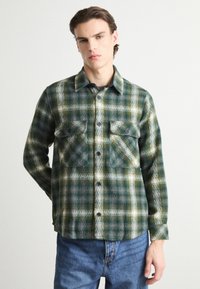 Green and white plaid flannel shirt with a button-up front, two chest pockets, and a collar. Soft texture and slightly loose fit.