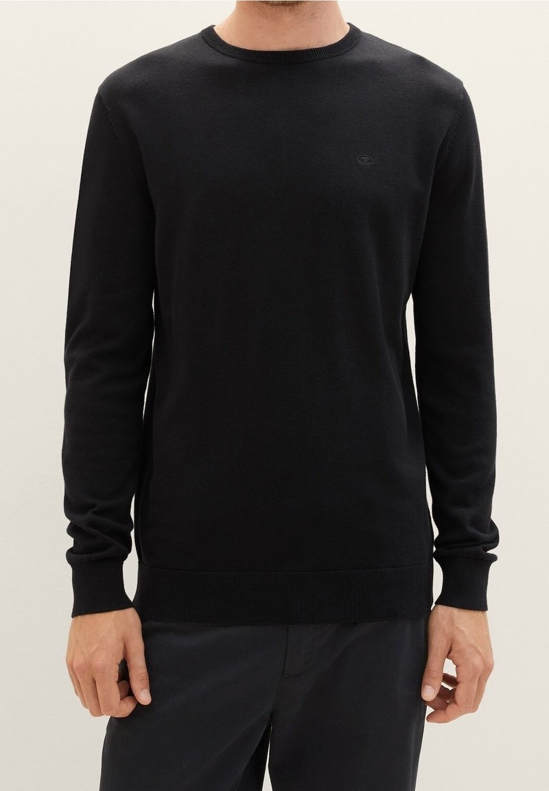 Maglione nero in maglia con scollo rotondo, maniche lunghe e polsini e orlo a coste. Presenta un piccolo logo sul petto. Texture liscia.