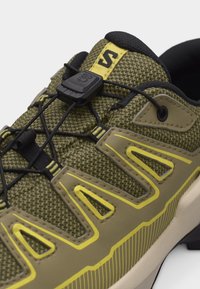 Κοντινό πλάνο πράσινου και κίτρινου αθλητικού παπουτσιού με επάνω μέρος από δίχτυ, κορδόνια με ελαστικό σχοινί και μαύρο κλείδωμα στην γλώσσα του παπουτσιού.