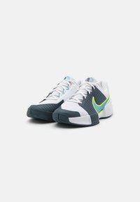 Hvite sportsko med grå detaljer, teksturerte paneler og en neongul swoosh. Har polstret krage og slitesterk gummisåle.
