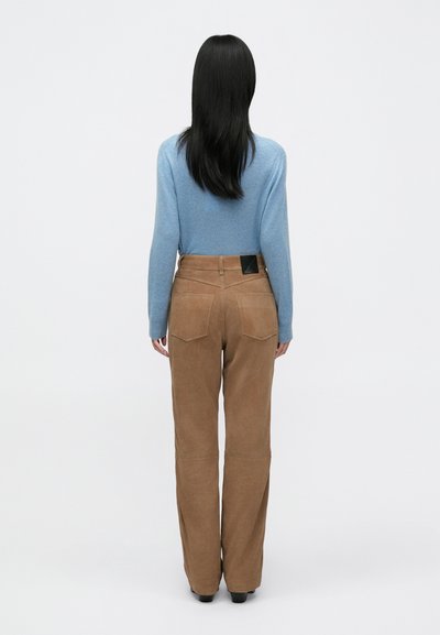 Tan suède wijde broek met achterzakken en zwart label detail, gecombineerd met een lichtblauwe trui met ronde hals. Zachte textuur, relaxte pasvorm.