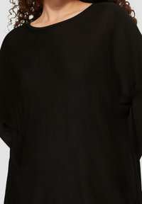 Schwarzer gestrickter Pullover mit weitem Ausschnitt und lässiger Passform. Strukturierter Stoff mit einem subtilen Muster, der drapierte Ärmel und Saum präsentiert.