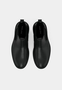 Pár černých hladkých kožených pánských slip-on bot s kulatými špičkami a poutky na bílem pozadí, s nápisem Pier One uvnitř.