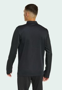 Μαύρο αθλητικό μπλουζάκι με μακριά μανίκια και λεία υφή, με γιακά και εφαρμοστή σχεδίαση. Όψη από την πλάτη; χωρίς σχέδια ή διακοσμητικά στοιχεία.