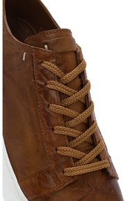 Bruine leren sneaker met bijpassende gevlochten veters en witte rubberen zool, met gedetailleerde stiksels en textuur.