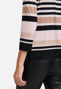 Gestreiftes Oberteil aus weichem Stoff mit horizontalen Linien in Schwarz, Beige und Pink. Enganliegende dreiviertel Ärmel und schwarze Hose.