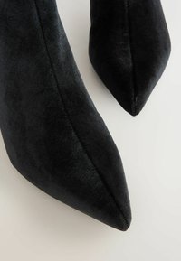 Melnas samtažas norādītā pirksta kurpes ir ar gludu tekstūru un elegantu dizainu, ar augstu stiletto papēdi, kas nodrošina elegantu izskatu.