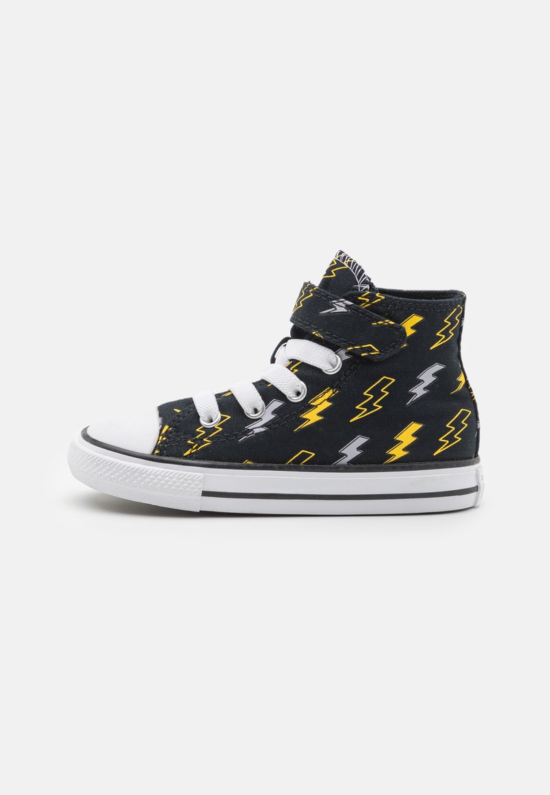 Zapatilla alta negra con un patrón de rayos amarillos y grises, tapa de punta de goma blanca y cordones blancos. Correa de velcro en el cuello.