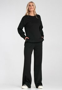 Czarna bluza i pasujące spodnie wykonane z miękkiego materiału. Bluza ma luźny krój z okrągłym dekoltem i bocznymi rozcięciami; spodnie mają prostą nogawkę.