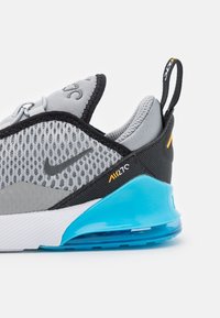 Grå och svart träningsskor med ovandel i mesh, blå detaljer och synlig dämpning. Har en svart dragflik och Nike-logotyp.