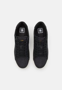 Černé džínové tenisky s texturovaným svrškem, kulatou špičkou, černými tkaničkami a bílou gumovou podrážkou. Na jazyku a boku je logo.