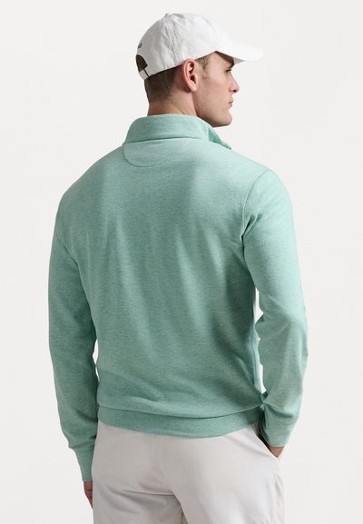 Mintgrön pullover i mjukt material, med hög krage och långa ärmar, i kombination med ljusa byxor.