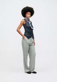 Tamsiai mėlyna be rankovių palaidinė su raukšlėtu akcentu, derinama su šviesiai pilkais dryžuotais kelnėmis ir juodais kniedžių apdaila bateliais.