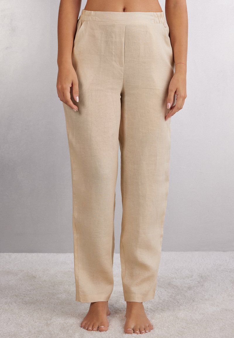 Beiga linbyxor med avslappnad passform, elastisk midja och sidofickor. Slät textur med subtilt vävningsmönster.