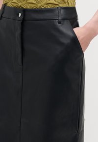 Crna kožna suknja s elegantnim dizajnom i suptilnim sjajem, bočnim džepovima i prednjim kopčanjem za uski kroj.