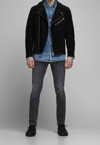 Svart mocka bikerjacka med silverfärgade dragkedjor, lager på en blå denimskjorta. Grå jeans och svarta skor fulländar outfiten.