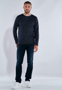 Dunkelblauer langer Pullover mit einem weißen Kragen, kombiniert mit dunklen Jeans und weißen Turnschuhen. Das Outfit weist ein klassisches, lässiges Design auf.