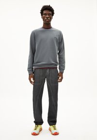 Sweatshirt gris à col rond, associé à un pantalon gris foncé avec des détails de couture visibles. Les chaussures sont jaunes avec des accents oranges et des semelles texturées.