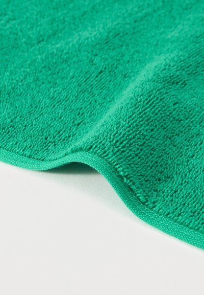 Κοντινό πλάνο διπλωμένου πράσινου μικροϊνικού πανιού που δείχνει την απαλή, υφή επιφάνειά του και τα ραμμένα άκρα σε λευκό φόντο.