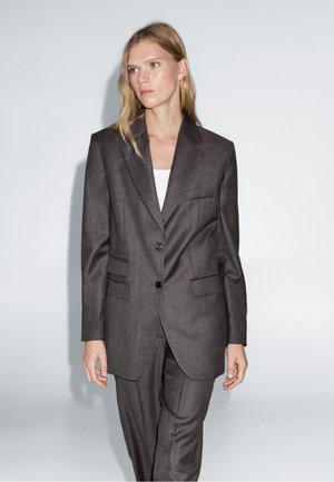 Costume sur mesure gris foncé avec une veste à un bouton, deux poches avant et un pantalon assorti. Tissu lisse avec une texture subtile.