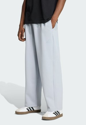 Lyseblå sweatpants med løs pasform, der har sidelommer og præget Adidas-logo. Kombineret med hvide sneakers og en sort skjorte.