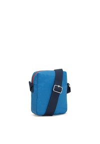 Blå kanvas crossbody-väska med rektangulär form, dragkedjestängning, marinblå rem och röd inredning. Har en framficka med detaljer i metall.