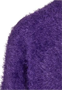 Pull violet en peluche avec une finition texturée et shaggy. Le tissu est doux et poilu, capturant la lumière et présentant une forme légèrement extensible.