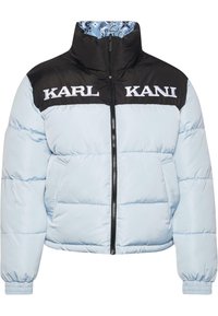 Gaiši zils pūkains jaka ar melnu augšējo paneli, ar baltu "KARL KANI" uzrakstu, augstu apkakli, rāvējslēdzēja priekšpusi un elastīgām aprocēm.