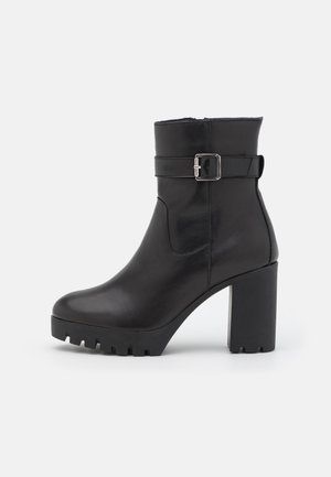 Zwarte leren enkellaars met een stevige hoge hak, voorzien van een zijgesp en een gestructureerde zool voor grip. Gladde afwerking en gestroomlijnd ontwerp.