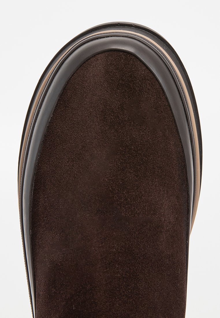 Mörkbrun mockaskos tå med slät läderdetalj och en lagerdämning i nyanser av brunt och svart.