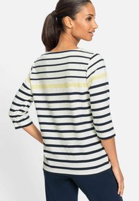 Gestreiftes Shirt mit drei Viertelärmeln in Beige mit dunkelblauen und gelben Streifen. Verfügt über einen runden Ausschnitt und einen weichen, leichten Stoff.