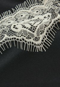 Černá látka s jemným bílým krajkovým lemem se květinovými vzory a delikátními třásněmi na okraji.