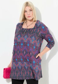 Lange mouw tuniek in donkergrijs met een kleurrijk ruitpatroon in rood, blauw en wit. Beschikt over een vierkante halslijn en zijzakken.