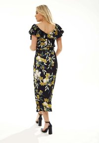 Floral black dress with ruffled off-the-shoulder sleeves, featuring yellow and pink flowers. Smooth fabric and form-fitting design. Black heels.