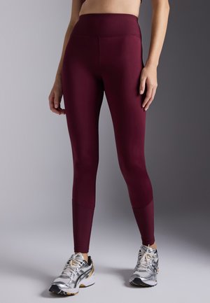 Maroon leggings with a ribbed high waistband, sleek fit, and smooth texture. Paired with silver running shoes featuring black accents.